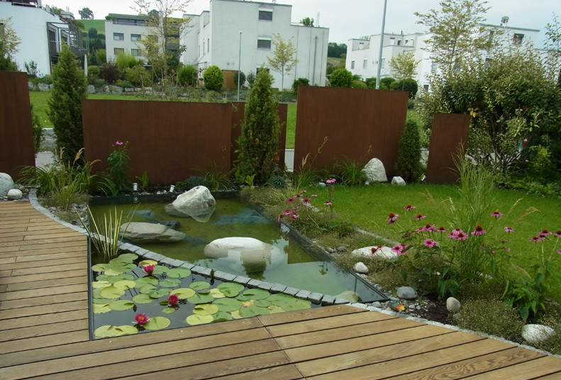 Étang de jardin naturel avec nénuphars et plantation, bordé d'une terrasse en bois