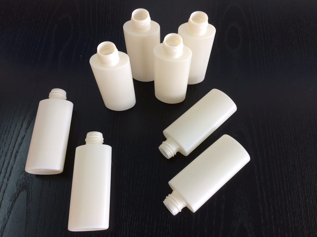 Eight white plastic bottles without caps on a dark table