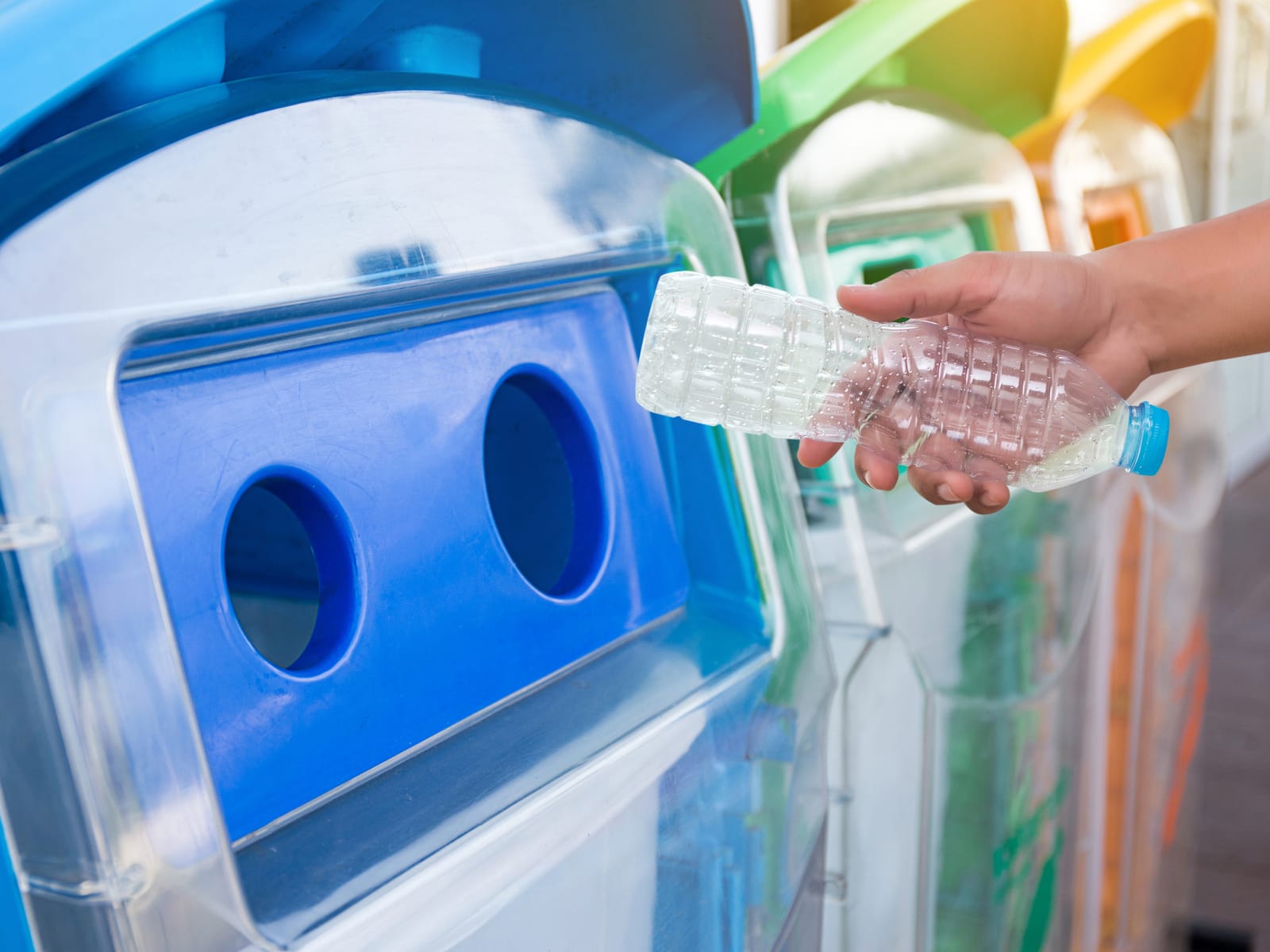 A hand drops an empty PET bottle into a blue collection bin