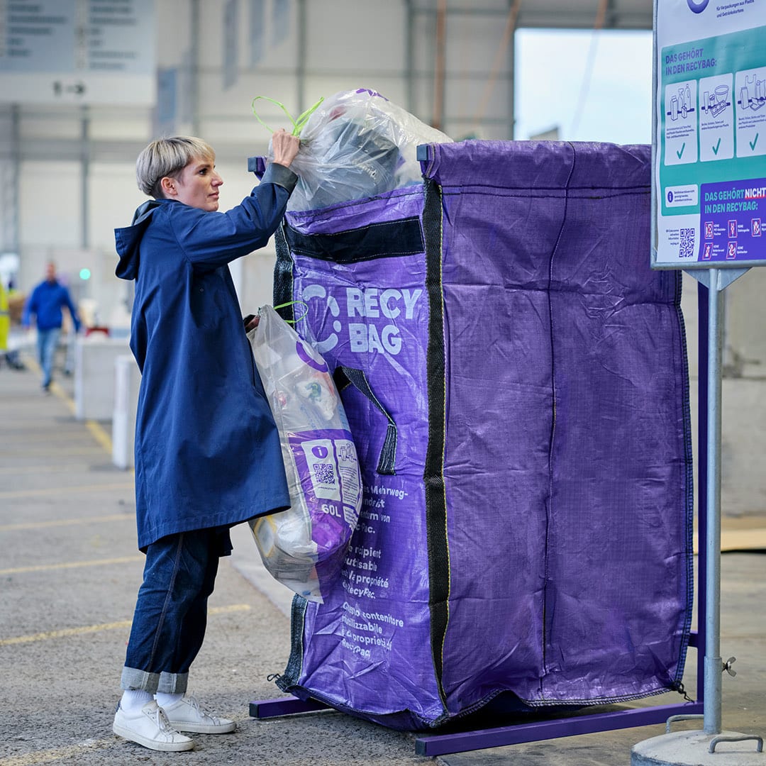 A person placing a filled collection bag into a purple RecyBag container