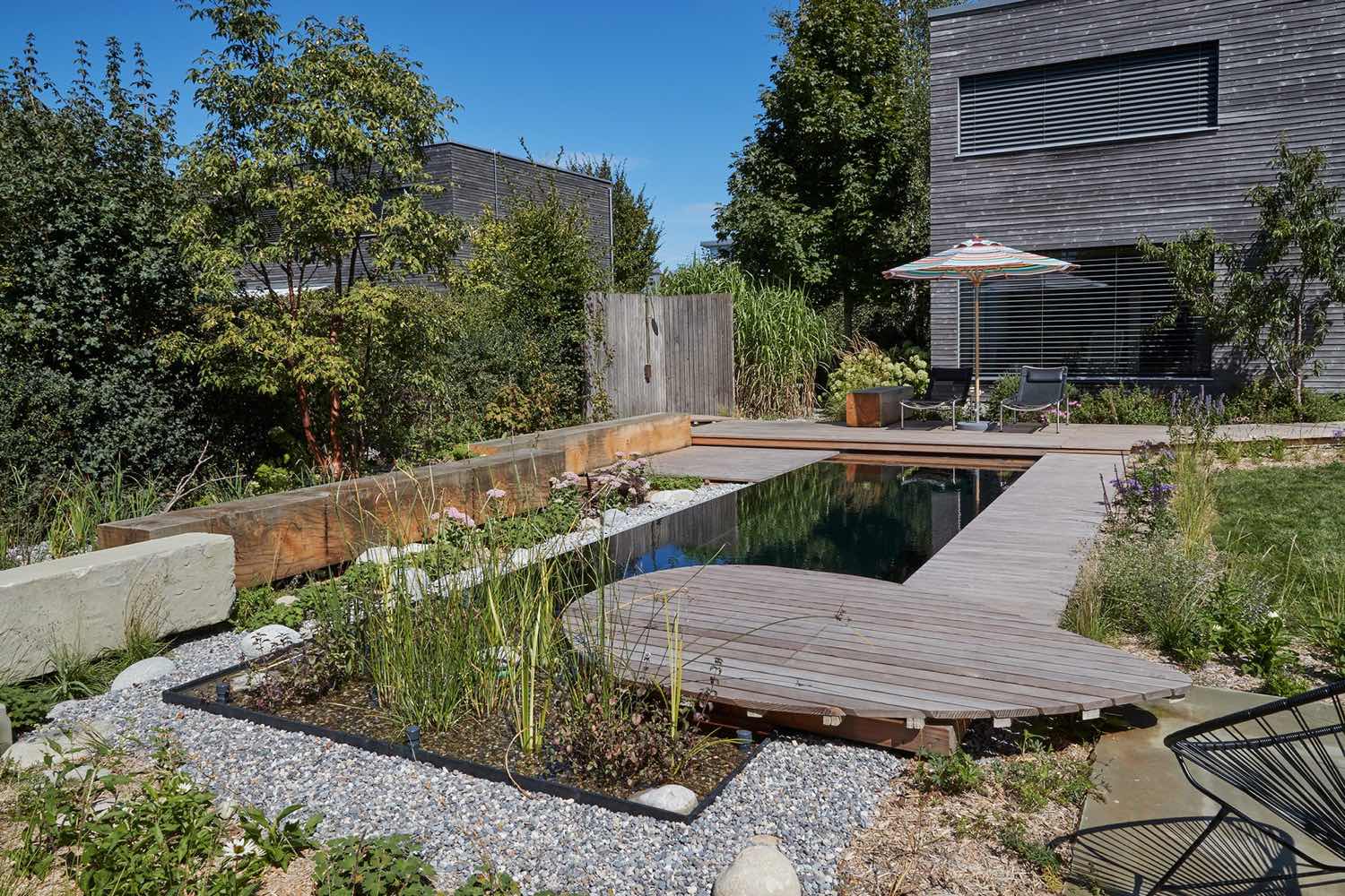 Biopool mit Holzsteg, dahinter Spielwiese und Wildhecke