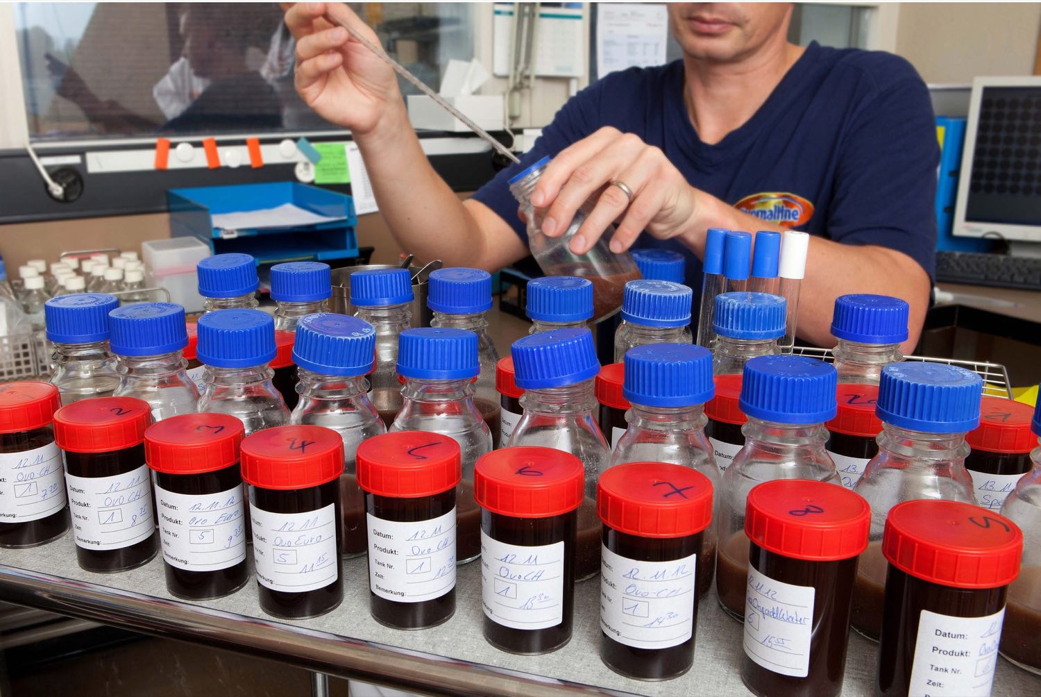 Laboratory technician with a row of labelled sample containers with red and blue lids