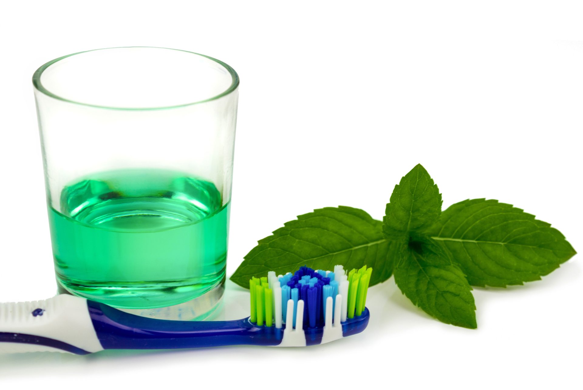 Verre de bain de bouche vert, à côté des brosses à dents et de la menthe fraîche
