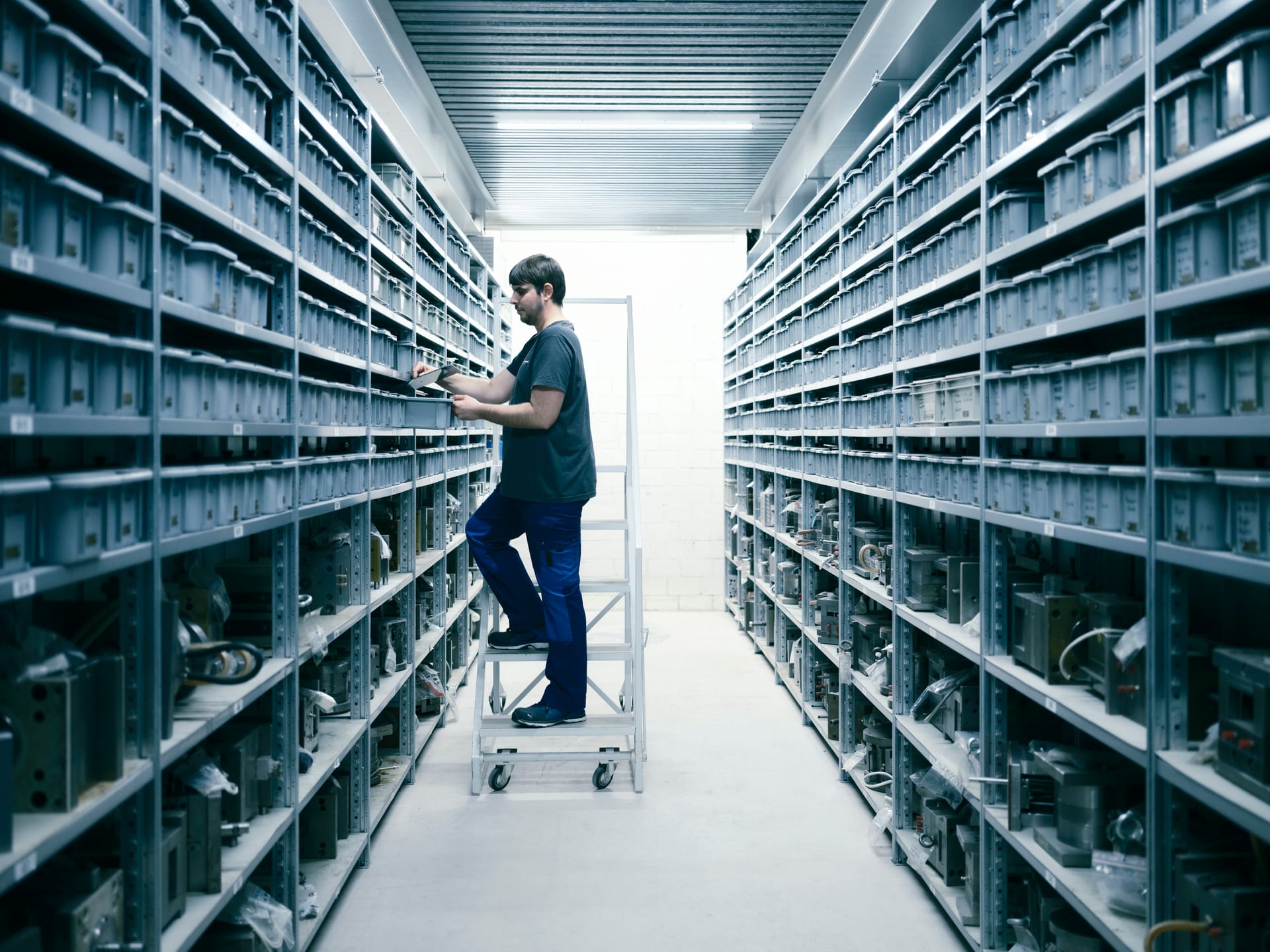 Long aisle in the tool archive with stored moulds, an employee on a step ladder in the aisle